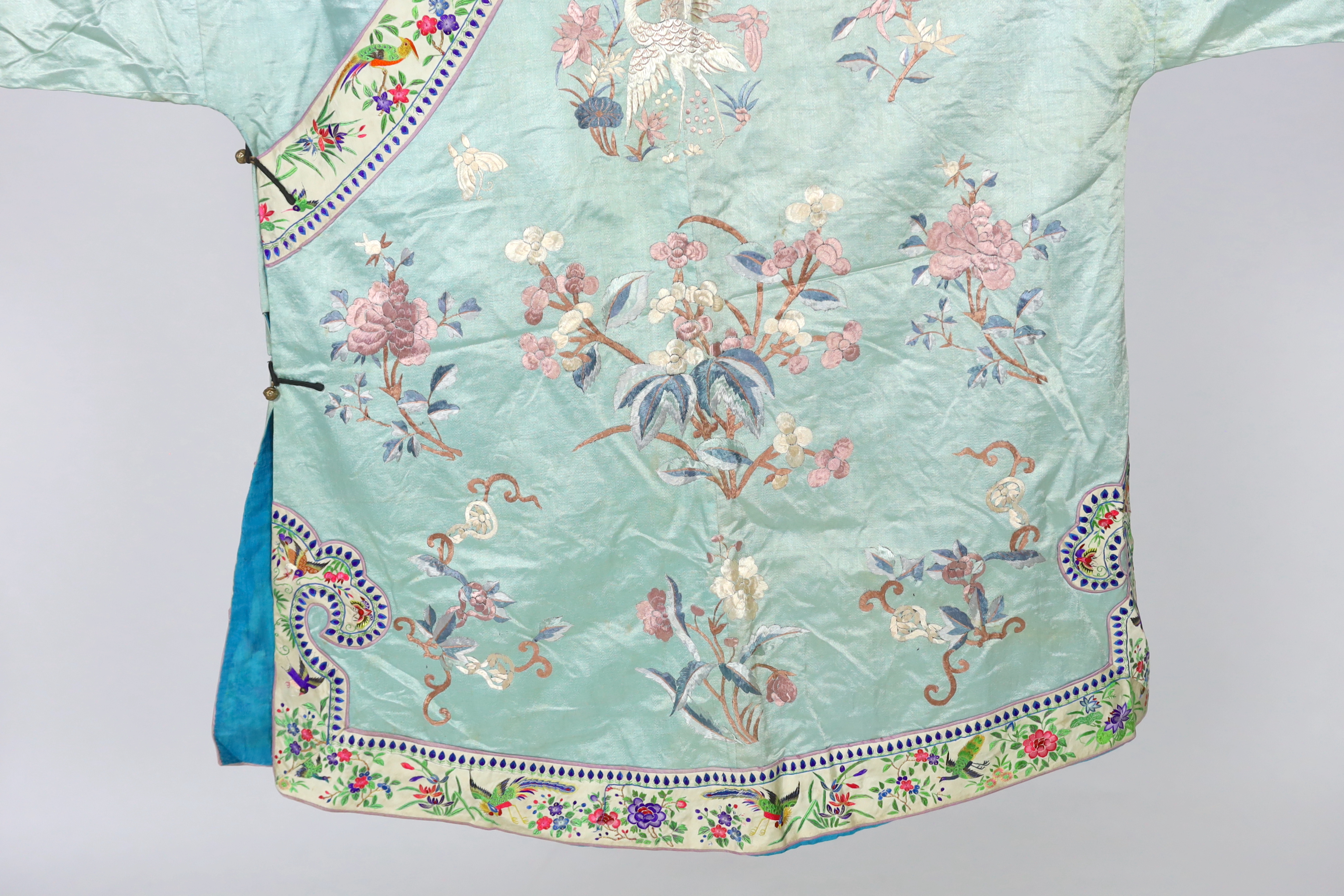 An early 20th century Chinese silk embroidered turquoise robe, embroidered in pastel silk with butterflies and flowers all over, polychrome embroidered braiding edged with lilac and bright pink sleeve bands embroidered w